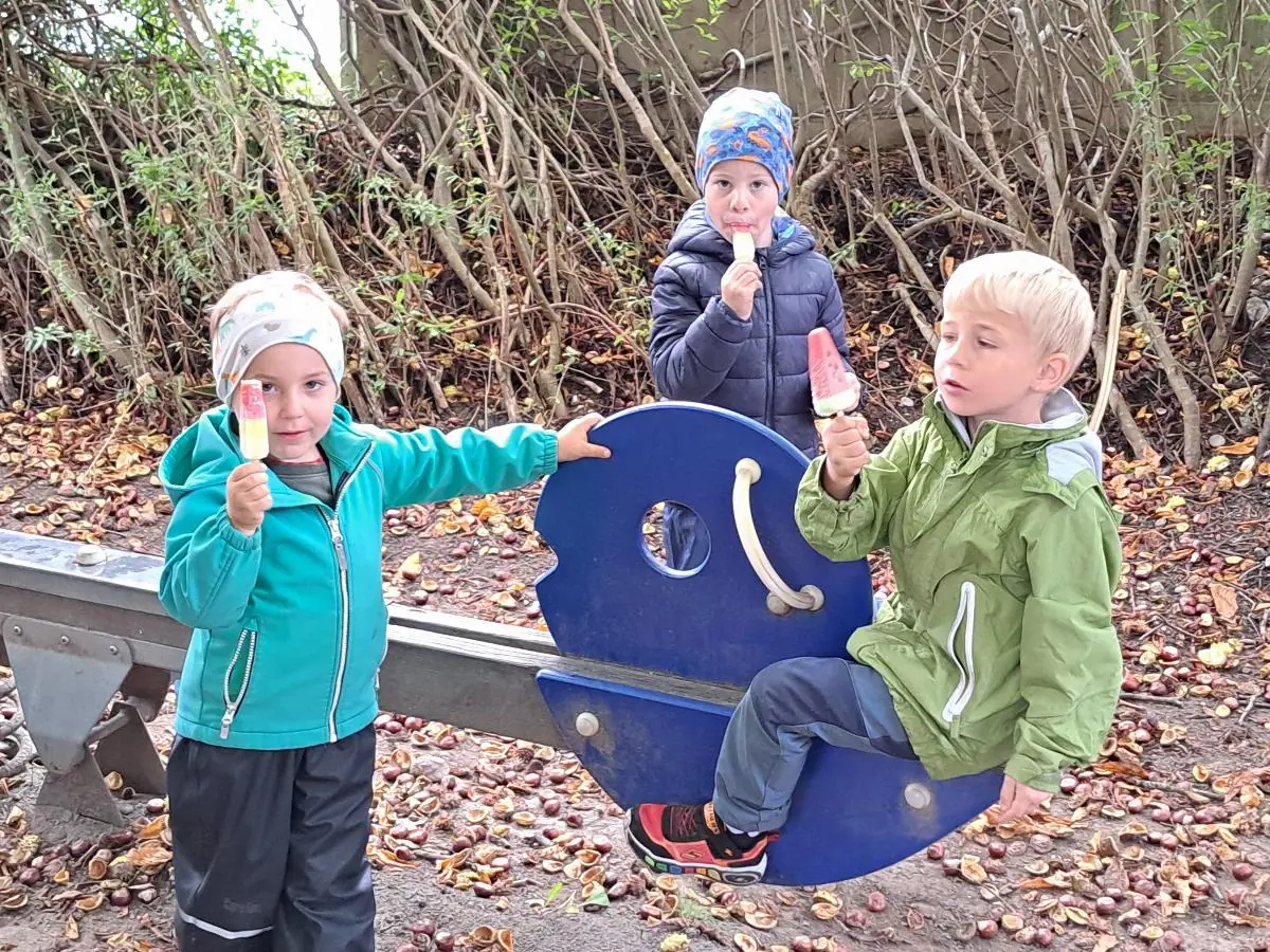 Drei Kinder spielen im Garten auf einem Wipptier.
