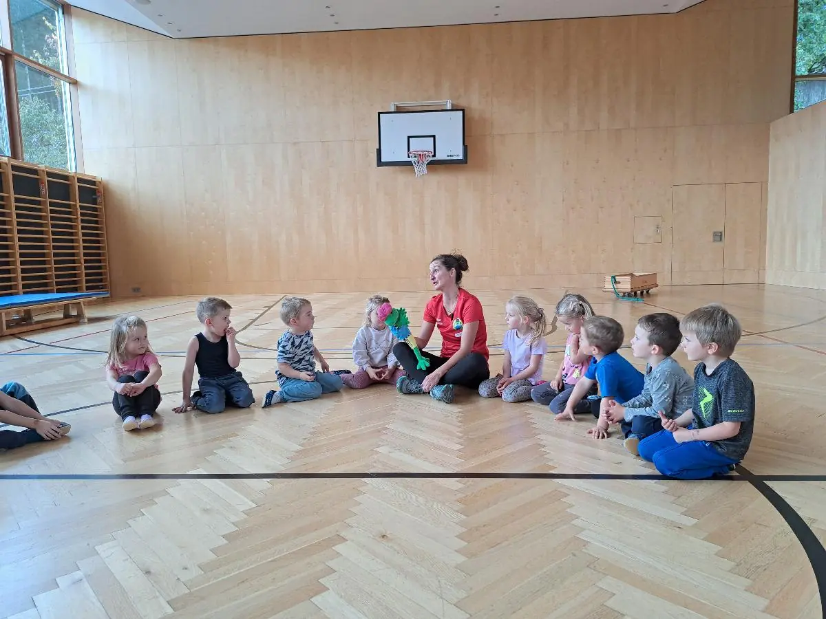 Kinder sitzen zum Bewegungsspiel im Turnsaal der Volksschule zusammen.